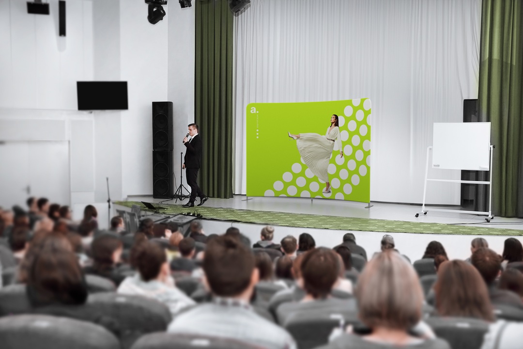 Prelegent występujący na scenie na tle ścianki reklamowej